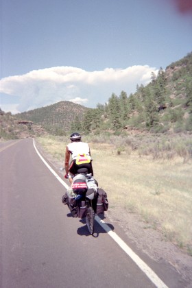 Adam riding away from camera with mushroom cloud over the hills
