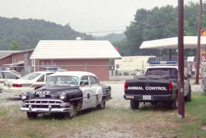 Old-time police car in back lot with other police cars