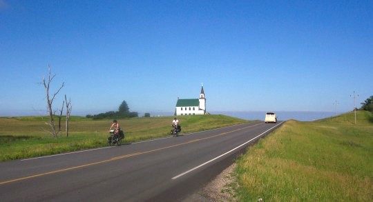 Dos ciclistas andando en bicicletas con una iglesia en la distancia