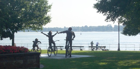 Sculpture of family of three cyclists in park with water in background