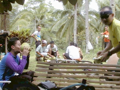 Cyclists drinking from coconuts with others in background cutting more open with a machete